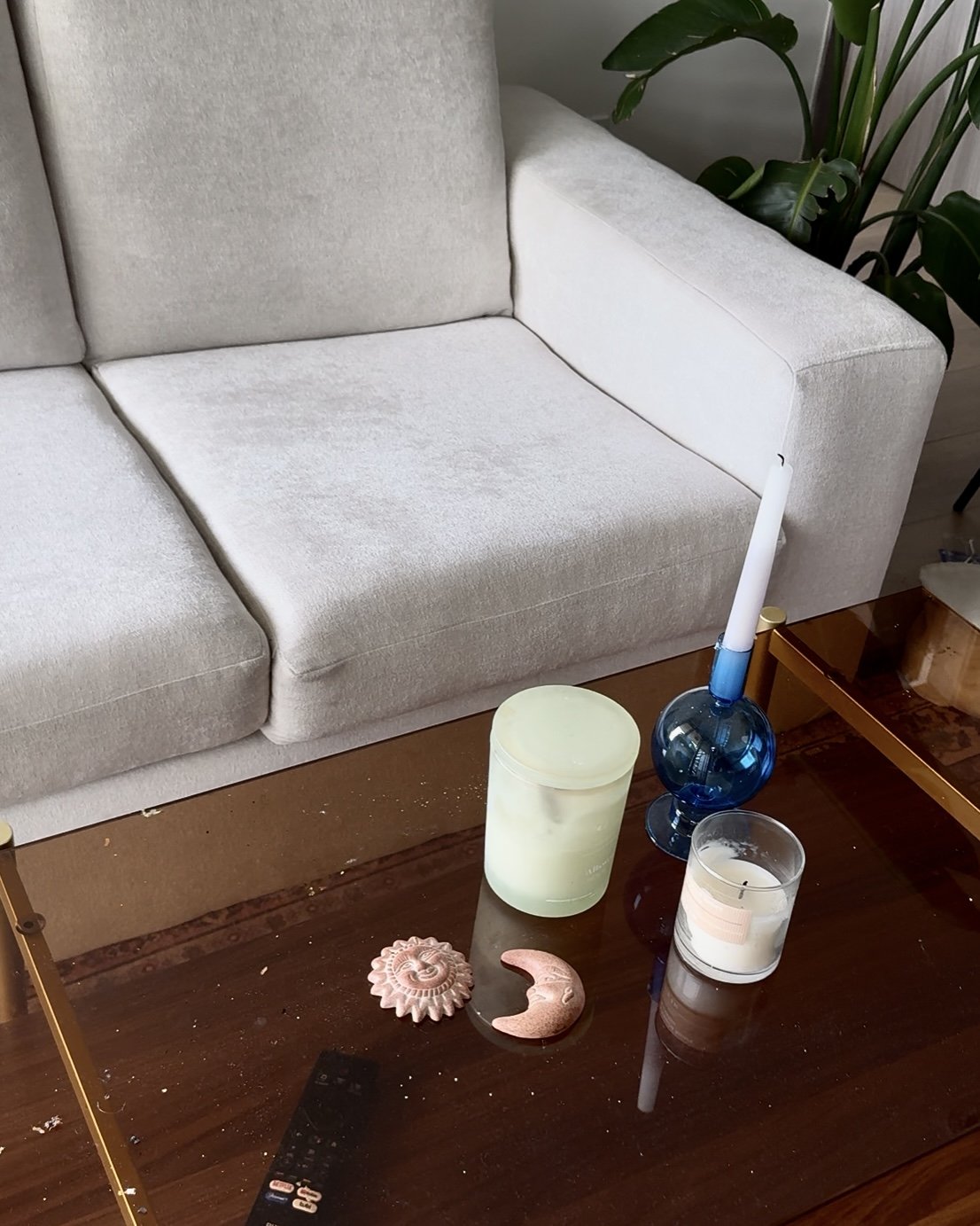 A beige sofa with a variety of candles and decorative objects on a wooden coffee table, including a blue glass vase with a candle, a white candle in a glass holder, a green candle, a sun-shaped figurine, a crescent moon figurine, and a remote control