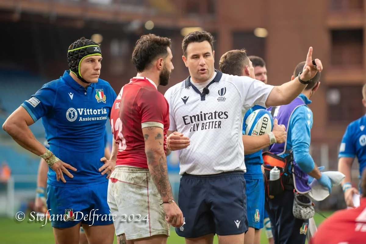 Rugby players and referee Ben O'Keeffe on a field engaged in conversation during a match.