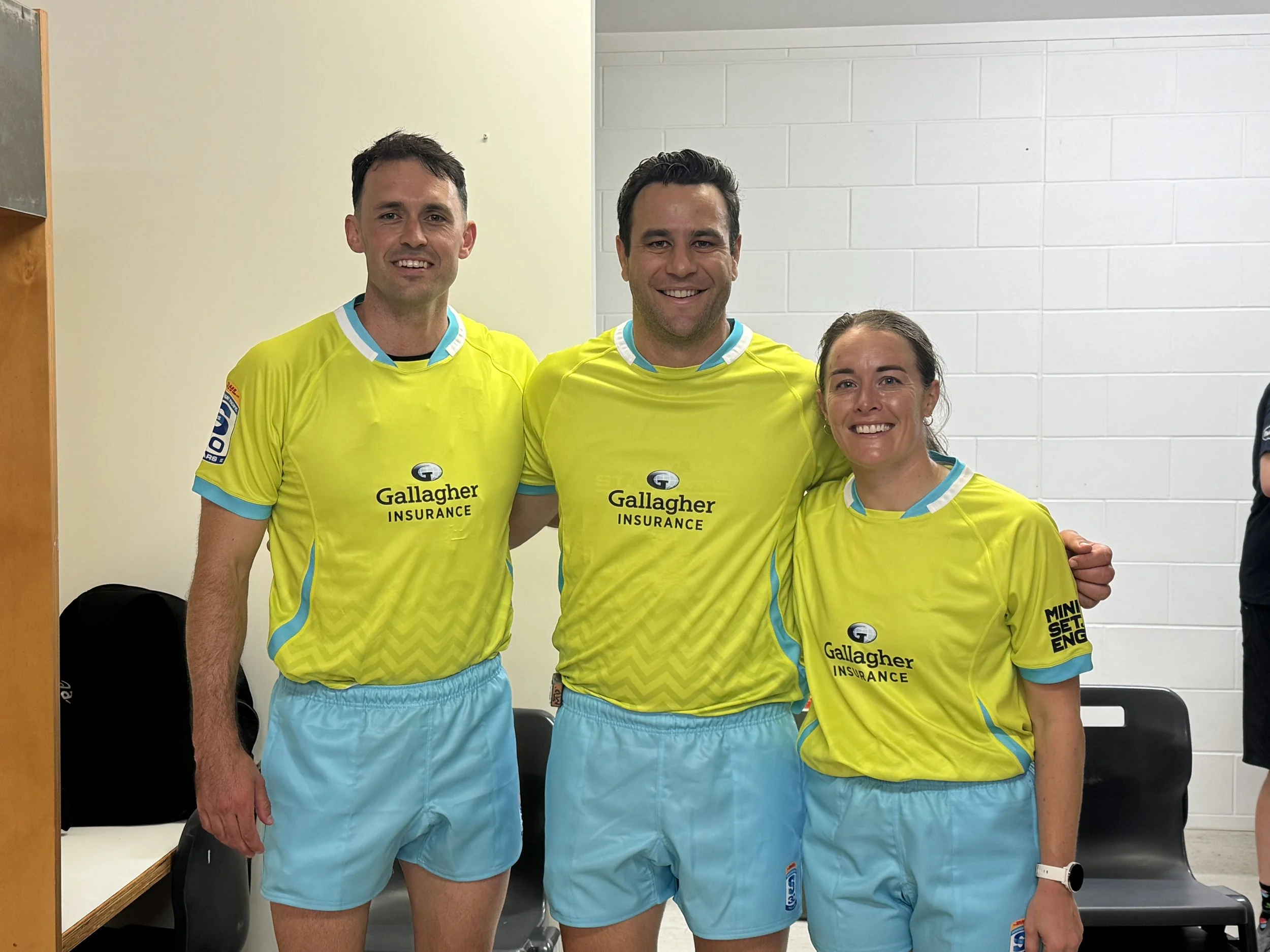 Three athletes including Ben O'Keeffe in a yellow and blue sports uniforms standing together indoors, smiling at the camera.