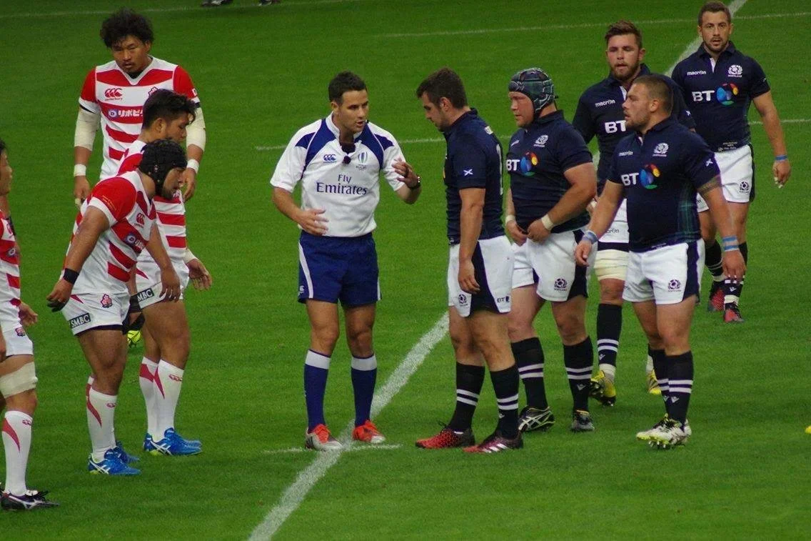Rugby players from two teams on the field, about to start a game, with an official referee Ben O'Keeffe in the center.