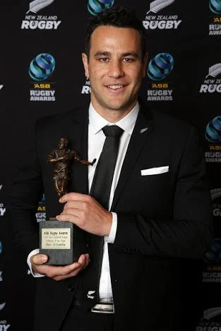 A man in a black suit holding a rugby referee award trophy, standing in front of a backdrop with New Zealand Rugby and ASB Rugby Awards logos - the winner was Ben O'Keeffe.