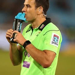 Rugby referee Ben O'Keeffe in a bright green jersey drinking from a blue sports water bottle during a match.