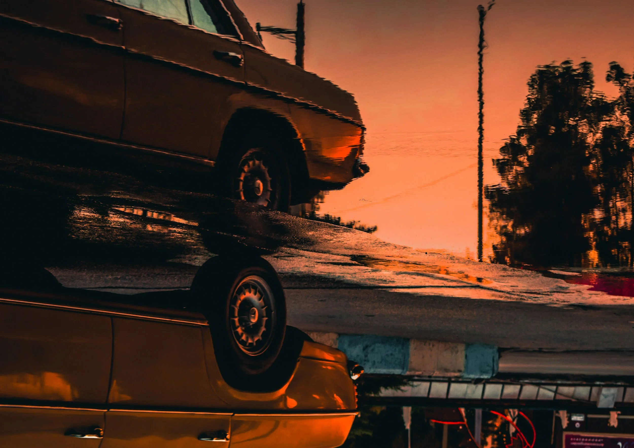 Reflection of a car parked on the street during sunset, with trees and utility poles in the background.
