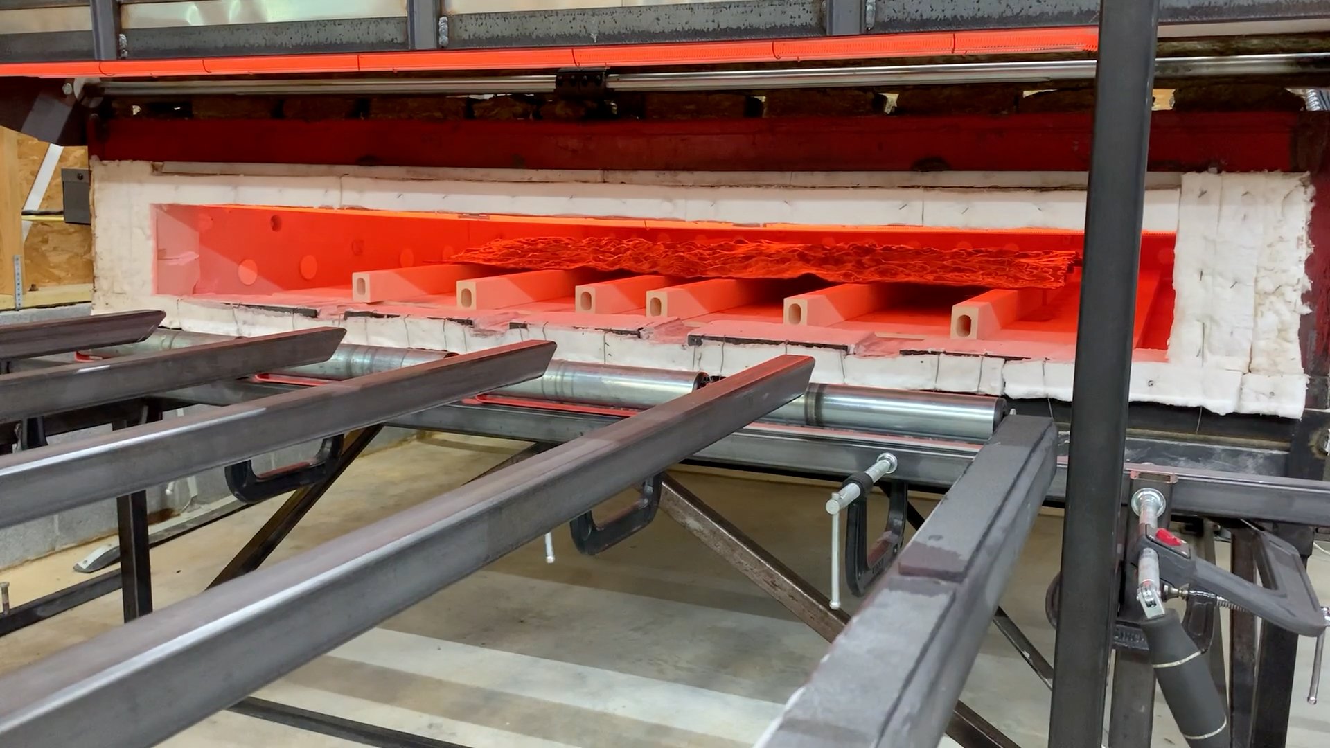 Industrial furnace with glowing red heat, metal rollers in front, and insulation around the opening