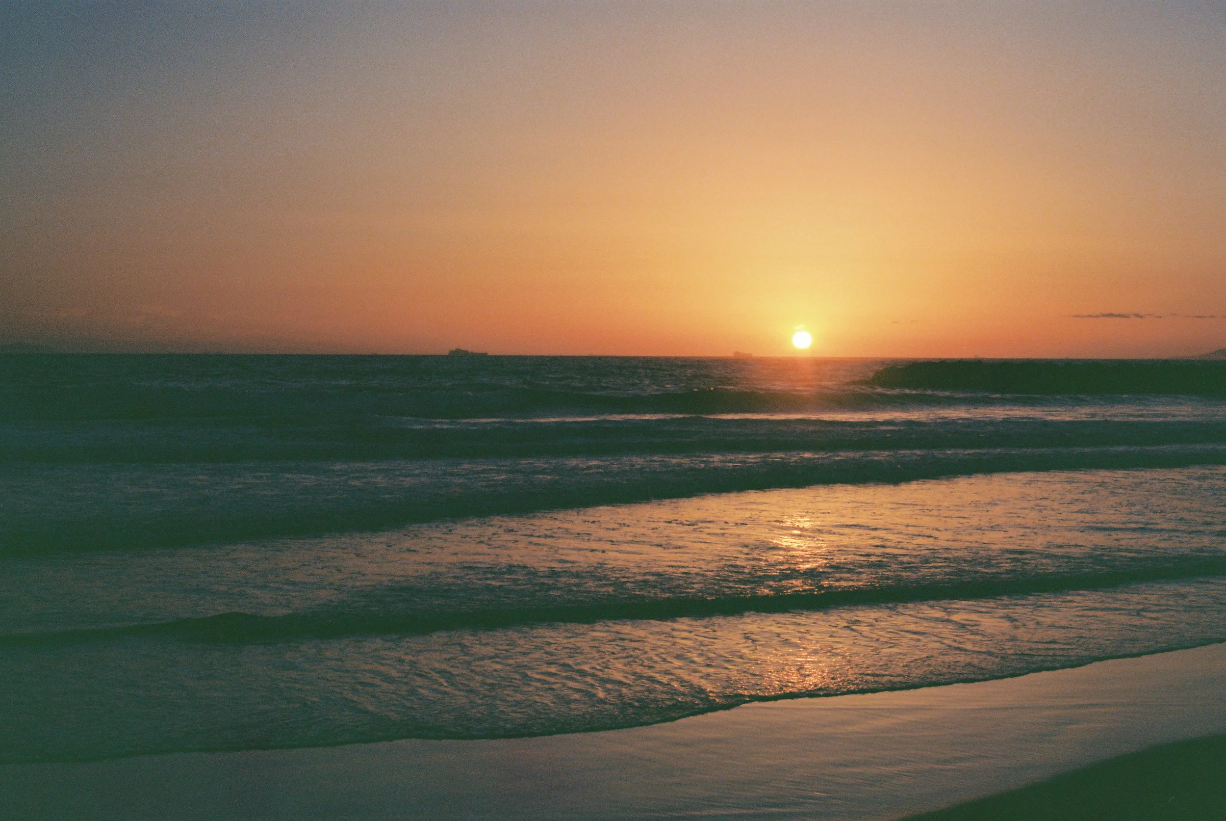 Sunset over the ocean with waves rolling onto the shore.