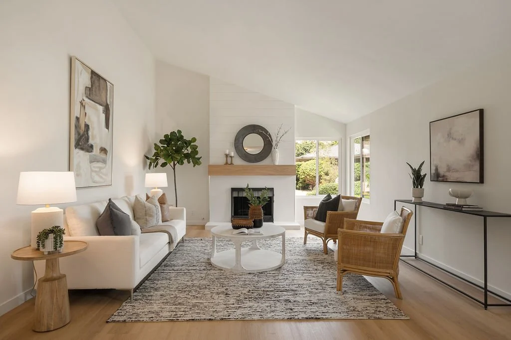 Bright living room with white walls and furniture, two windows, a fireplace, modern abstract art, and a mix of natural and neutral decor.