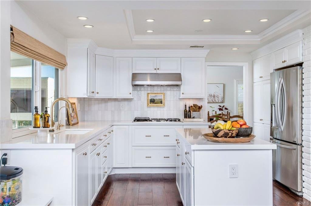 Bright white kitchen with stainless steel refrigerator, white cabinets, and a central island with fruit.