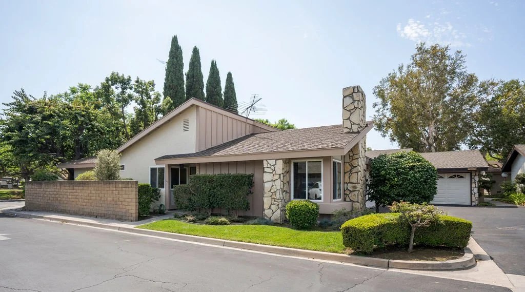 A suburban house with a brick and stone exterior, surrounded by well-maintained bushes and trees, with a driveway and a garage.