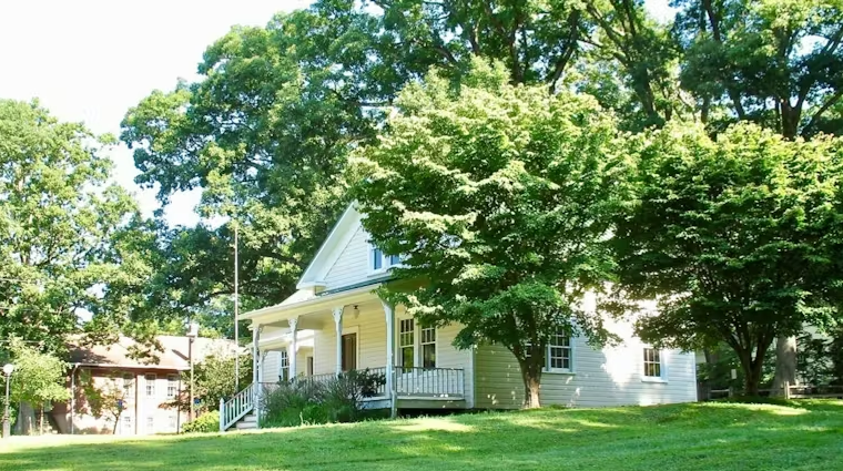 A white house with a porch surrounded by green trees and a well-maintained lawn.