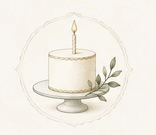 A white birthday cake with a single lit candle on top, decorated with gold accents, and accompanied by green leaves on a cake stand.