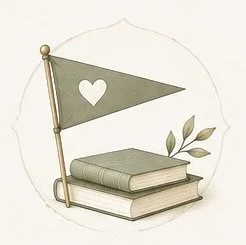 A small army green flag with a white heart symbol on a pole, placed atop two stacked closed books, with a leafy plant nearby.