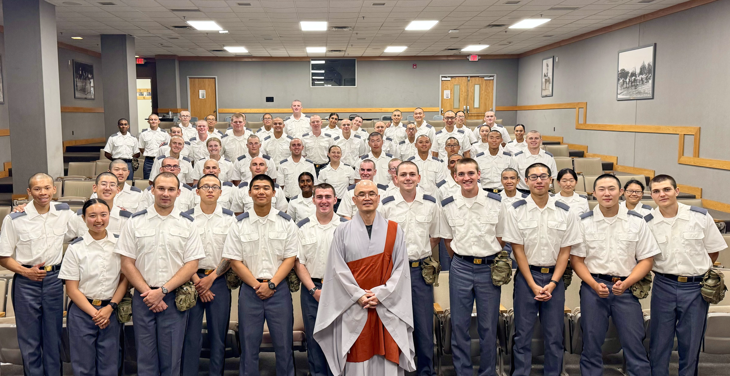 Group of uniformed individuals in a lecture hall with a Buddhist monk in the front center.