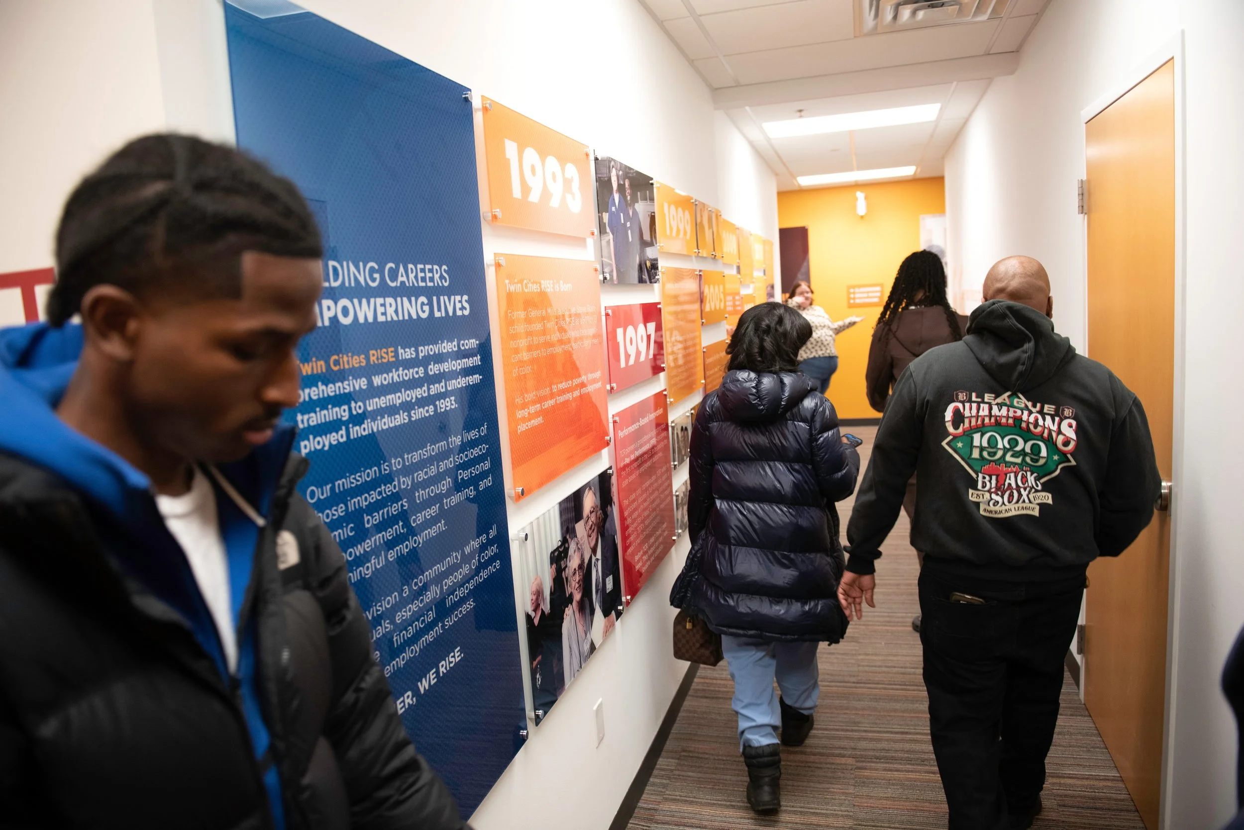 People walking down a hallway with display panels on the wall featuring historical years and information.