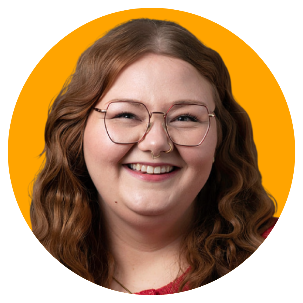 A young woman with wavy red hair, wearing glasses and a nose ring, smiling against a yellow background.
