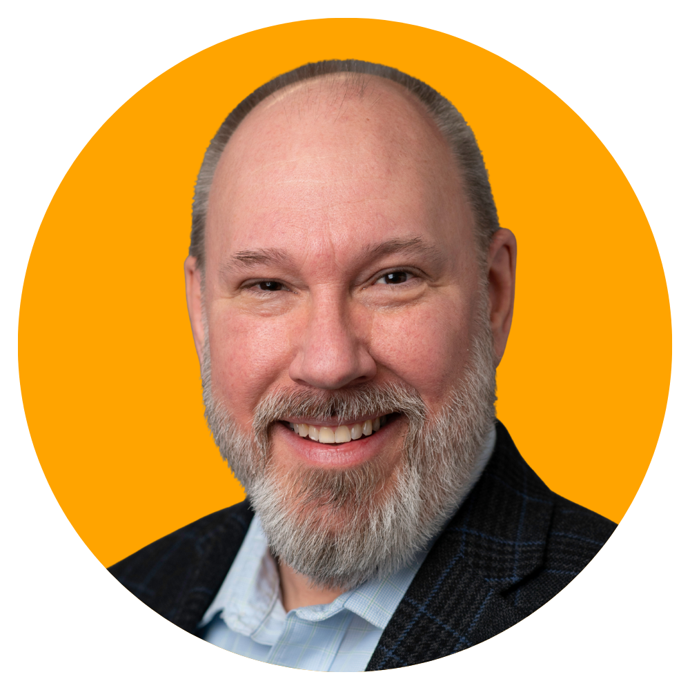 A smiling middle-aged man with a beard, dressed in a suit, against an orange circular background.