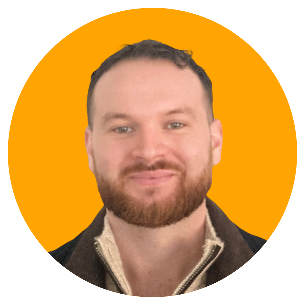 A man with a beard and short hair smiling, wearing a jacket and a light-colored zipper shirt, against an orange background.
