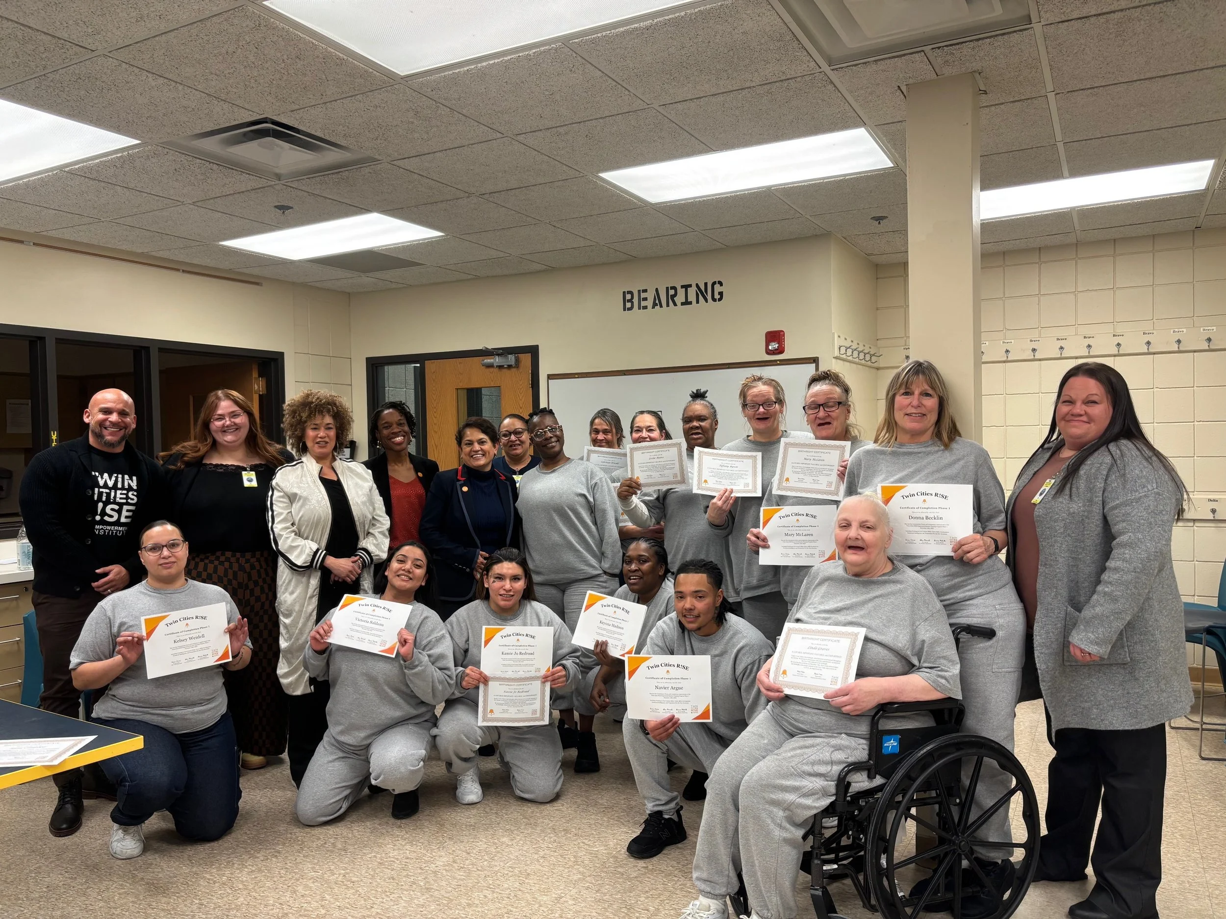 Group of diverse women and men smiling and holding certificates in a room celebrating achievements.