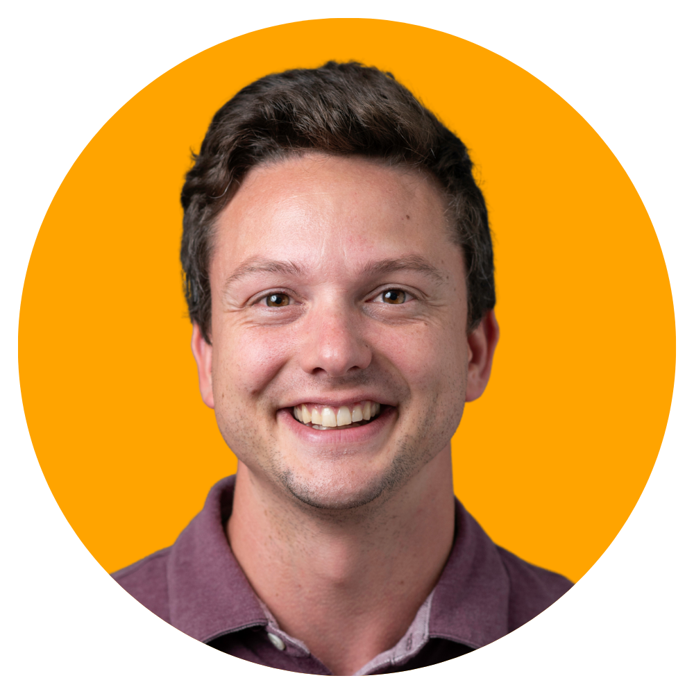 A smiling young man with short brown hair, wearing a maroon collared shirt, against an orange background.