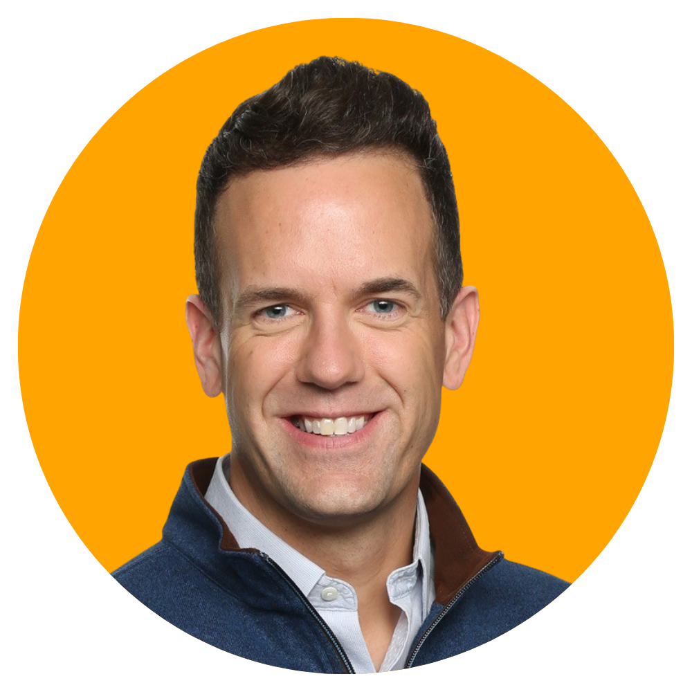 Portrait of a smiling man with short dark hair, wearing a white collared shirt and a dark jacket, against an orange background.