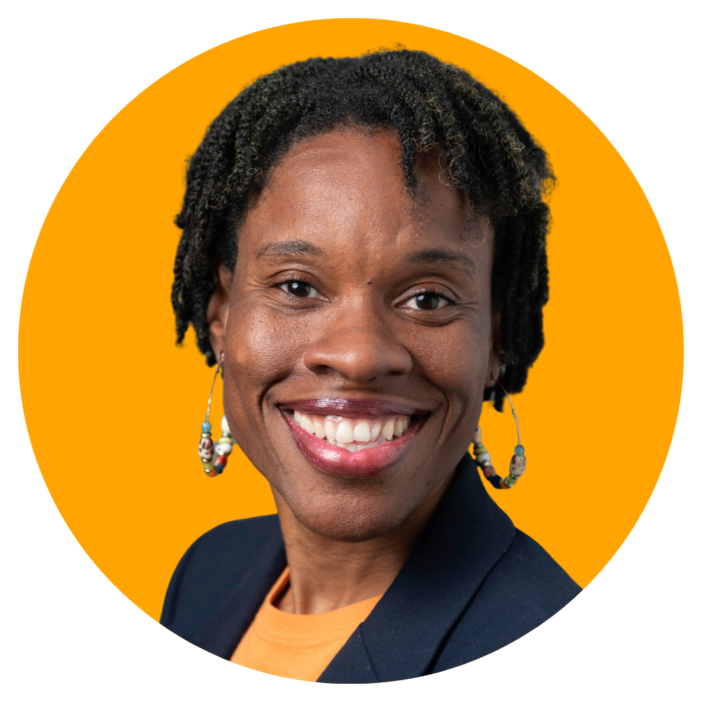Portrait of a smiling Black woman with short, dreadlocked hair, wearing earrings and a dark blazer against an orange background.