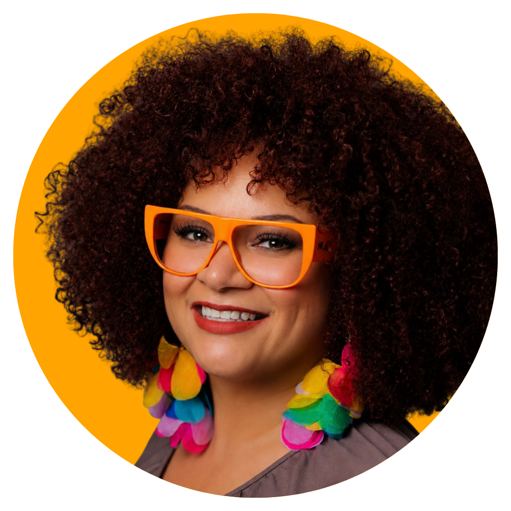 A woman with curly dark hair styled in a large afro, wearing orange glasses, colorful flower earrings, and smiling in front of a bright yellow background.