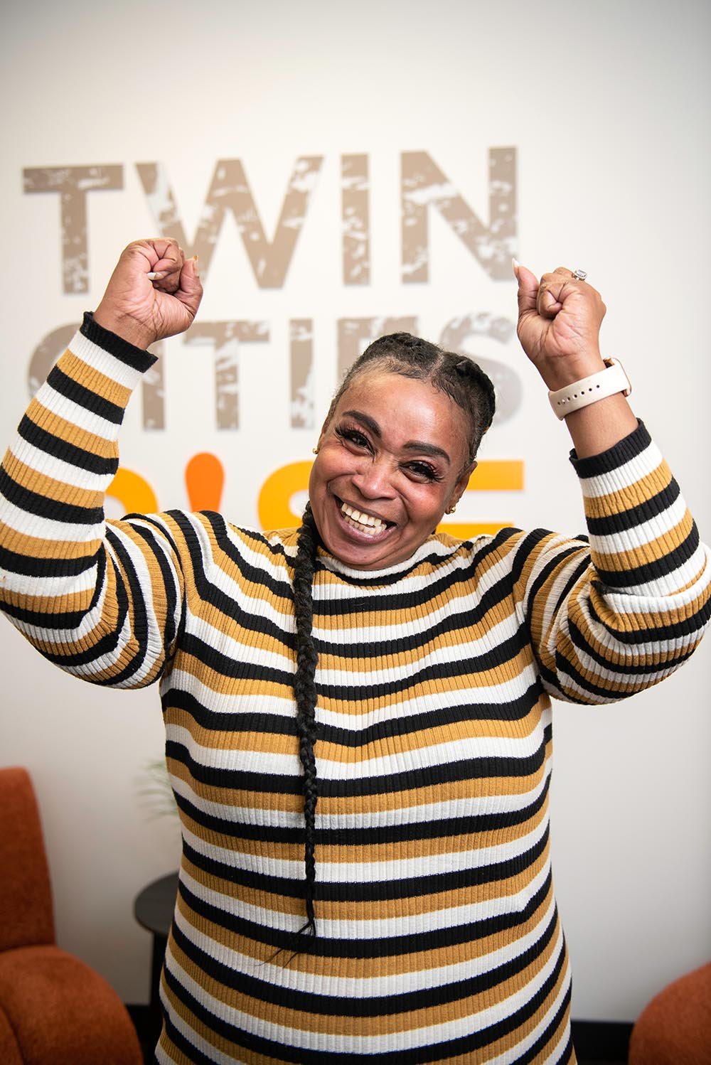 Woman smiling and flexing her arms inside an office with Twin Cities RISE's logo on the wall behind her.