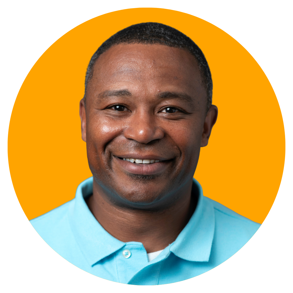 Close-up of a smiling man with dark skin, short black hair, wearing a light blue collared shirt against an orange background.