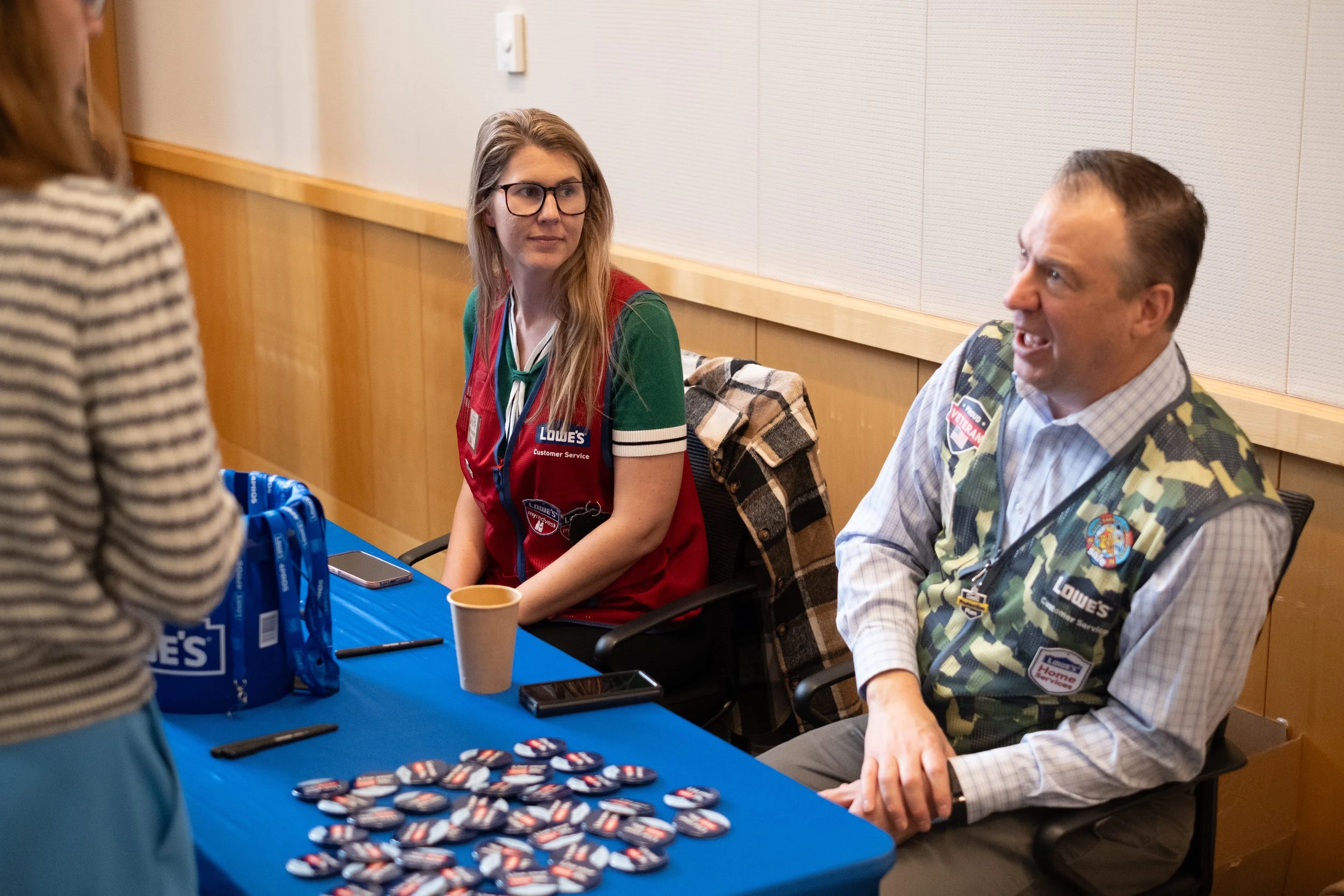 People participating in a community event, sitting at a table with buttons and promotional items, engaging in conversation.