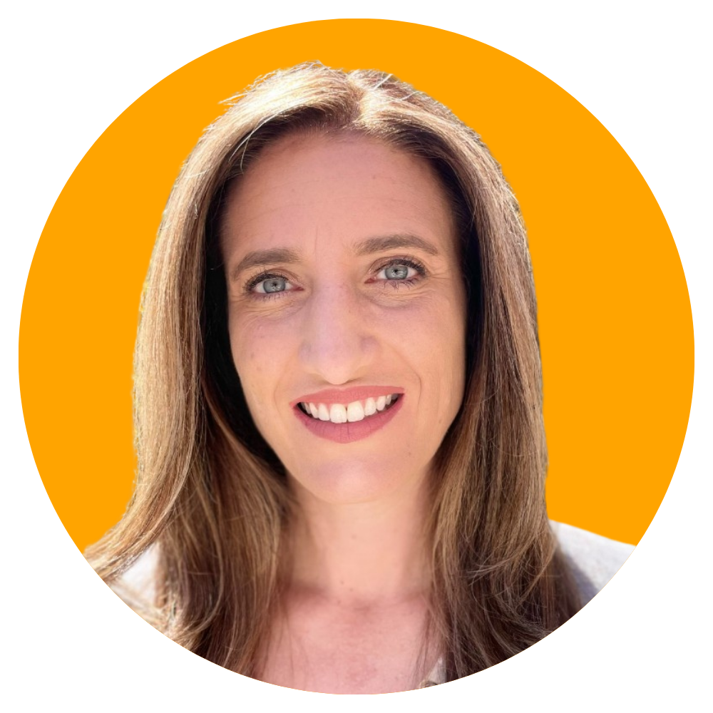 A woman with long brown hair, blue eyes, and a bright smile, looking directly at the camera, set against an orange background.