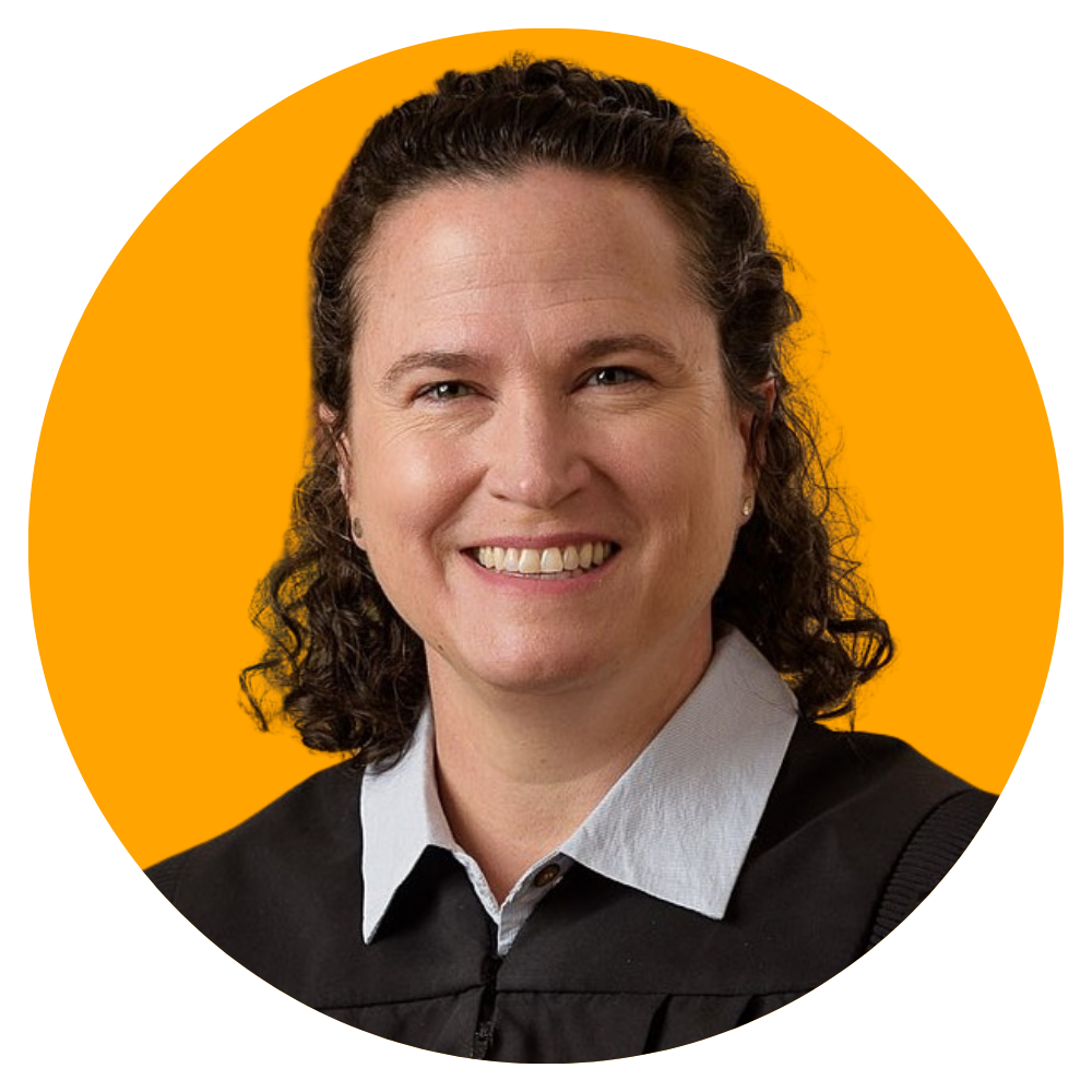 A woman with curly dark hair smiling, wearing a black and white outfit, in front of an orange background.