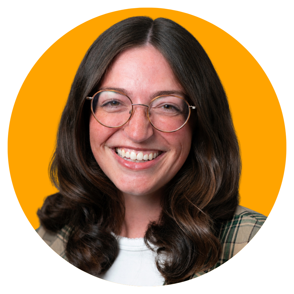A woman with long brown hair, wearing round glasses, smiling in front of a bright orange background.