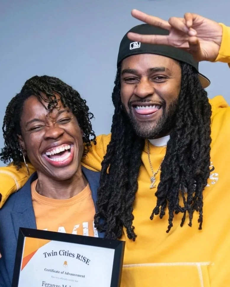 Two people celebrating, one woman and one man, smiling and making peace signs. The woman is holding a certificate of advancement from Twin Cities RISE