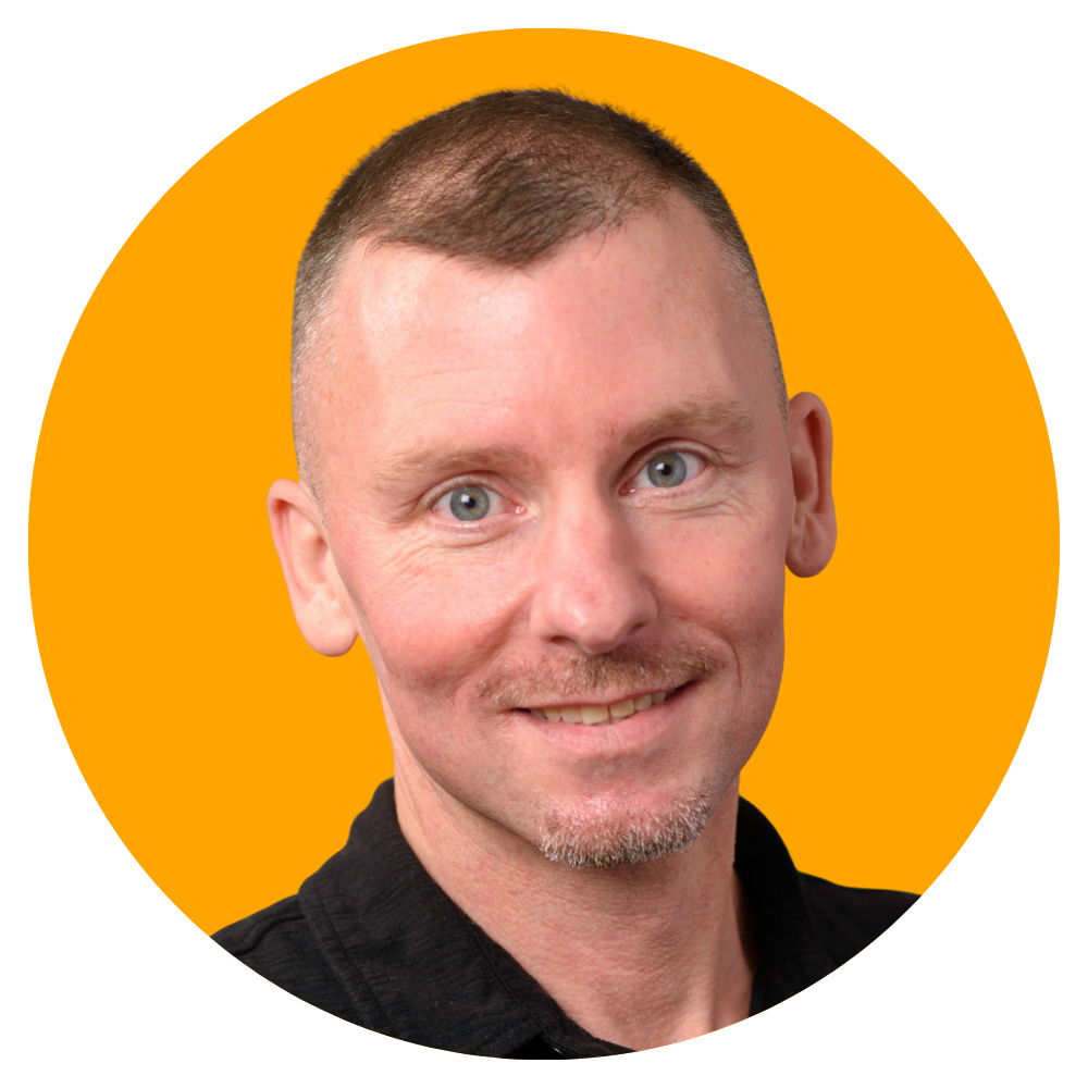Portrait of a smiling man with short brown hair and blue eyes, wearing a black shirt, against a yellow circular background.