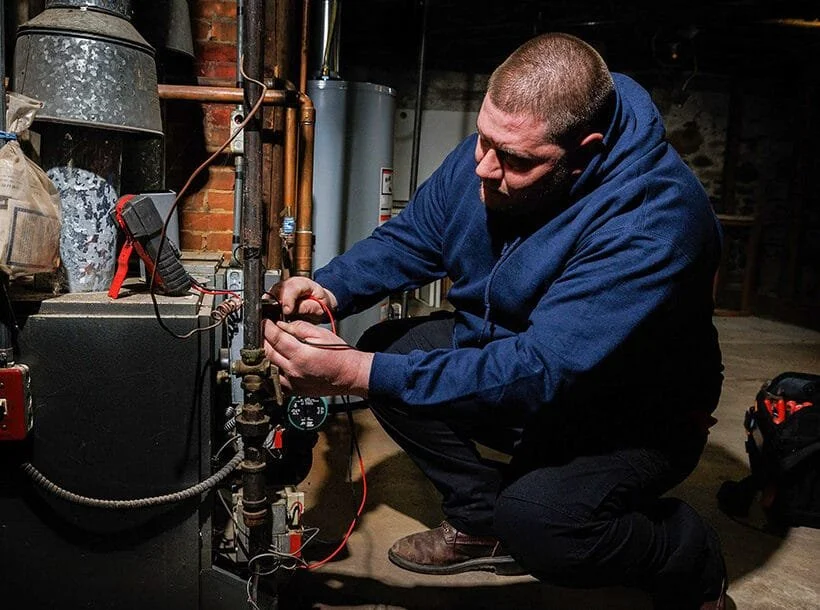 Man working on a mechanical or plumbing system in a basement or utility area.