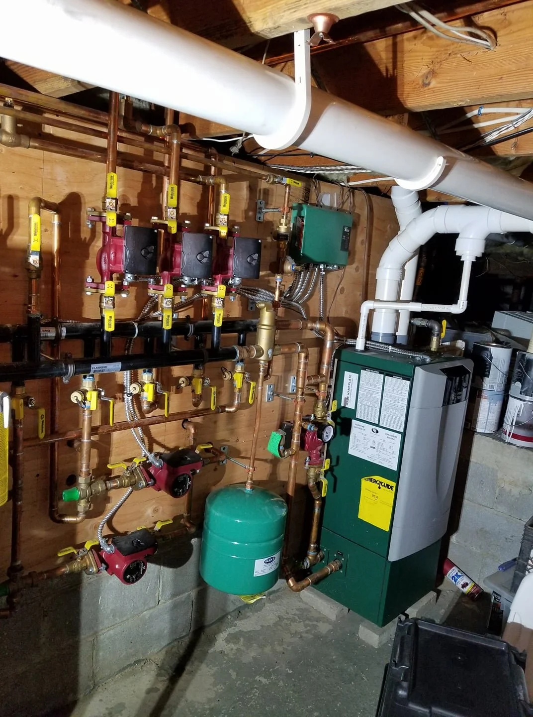 Mechanical room with copper and plastic pipes connected to a green boiler and a green water pressure tank.