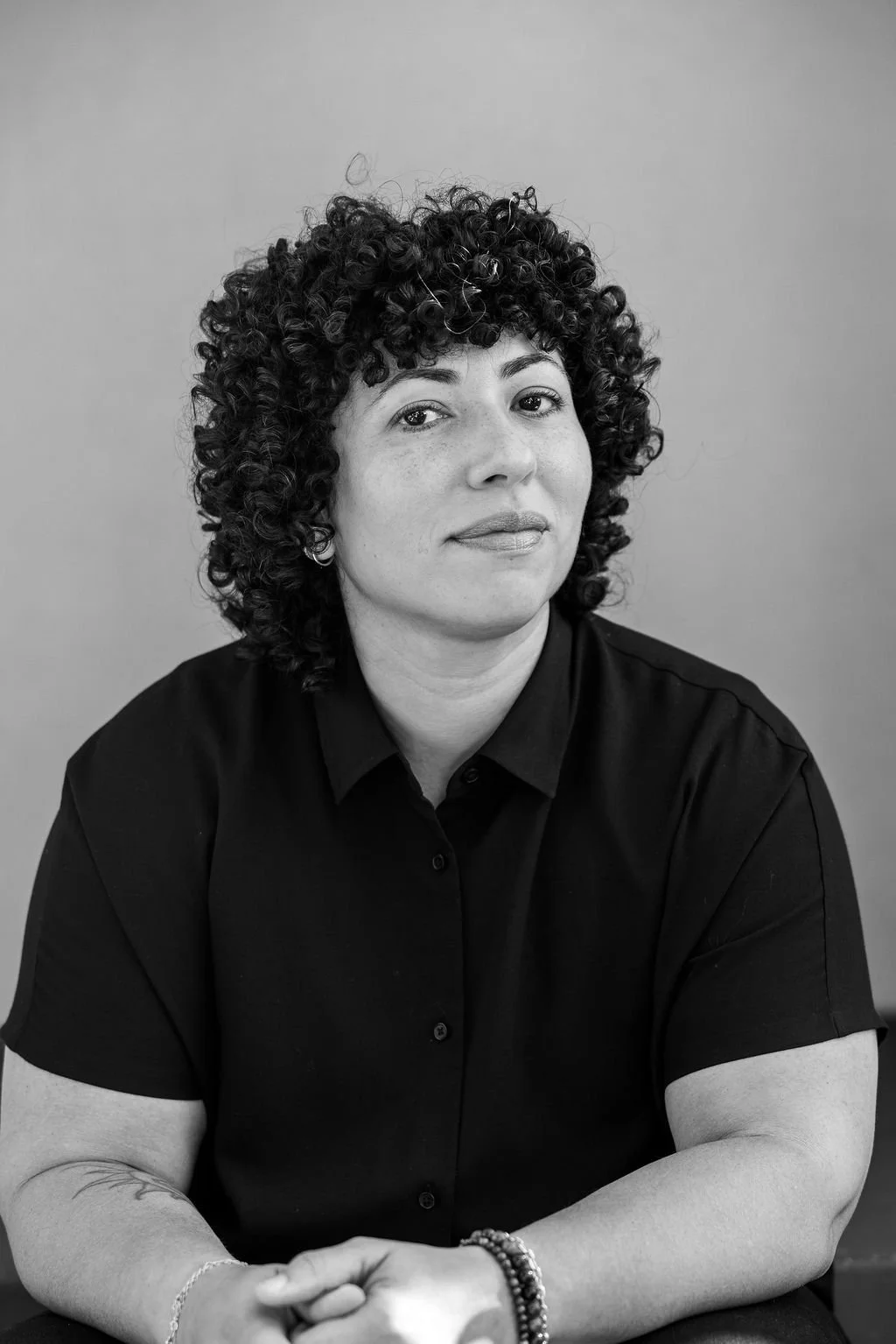 Black and white portrait of a woman with curly hair, wearing a dark shirt, looking confidently at the camera against a plain background.