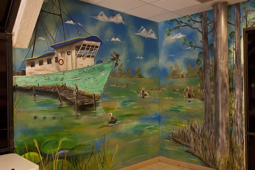 A large mural painting of a boat named 'Craw Daddy' docked at a weathered pier in a swampy area, with waterfowl and two people fishing in the water, surrounded by trees and marshland.
