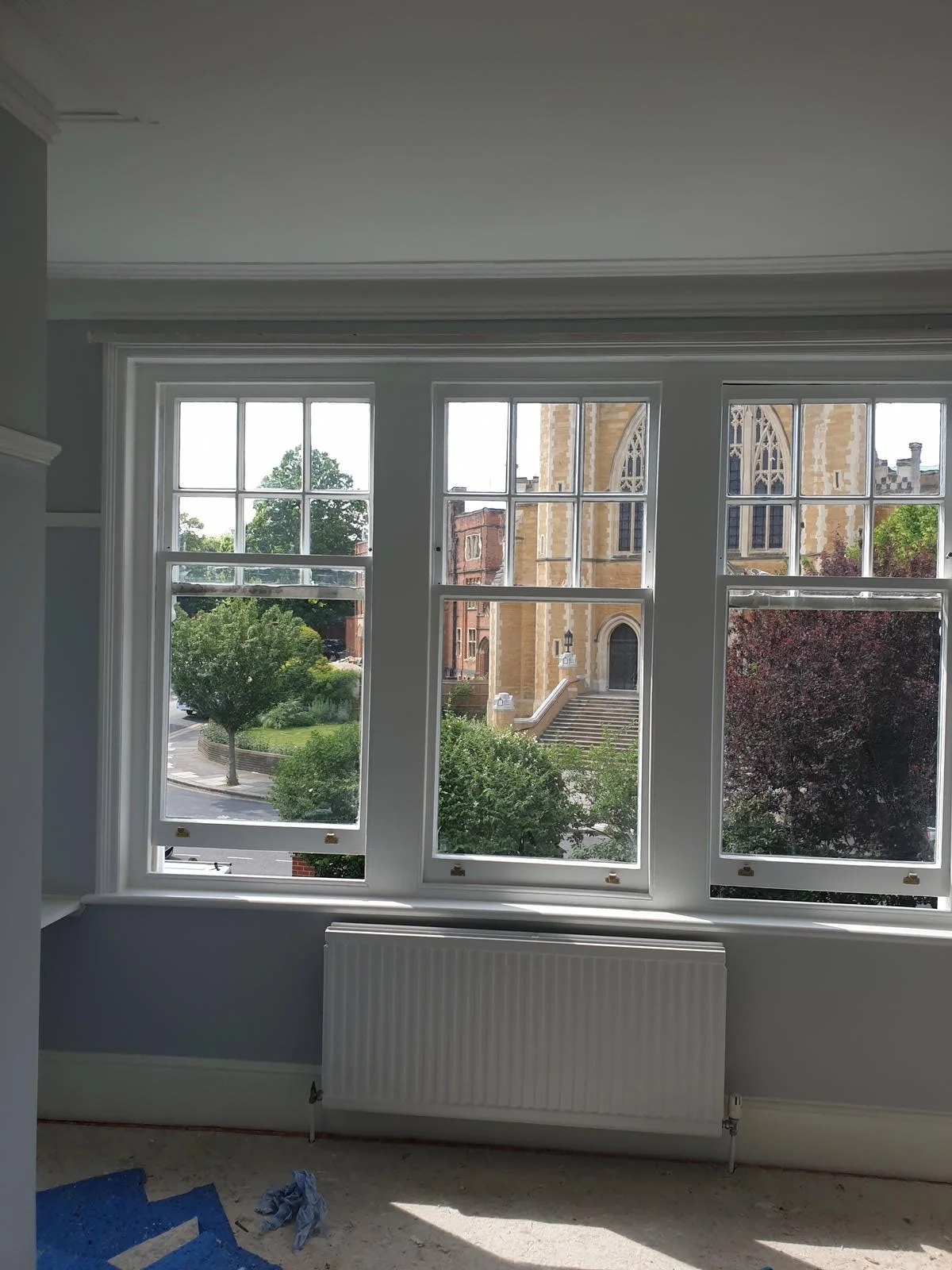 Interior view of a room with three large multi-pane windows overlooking a street with trees and a church.