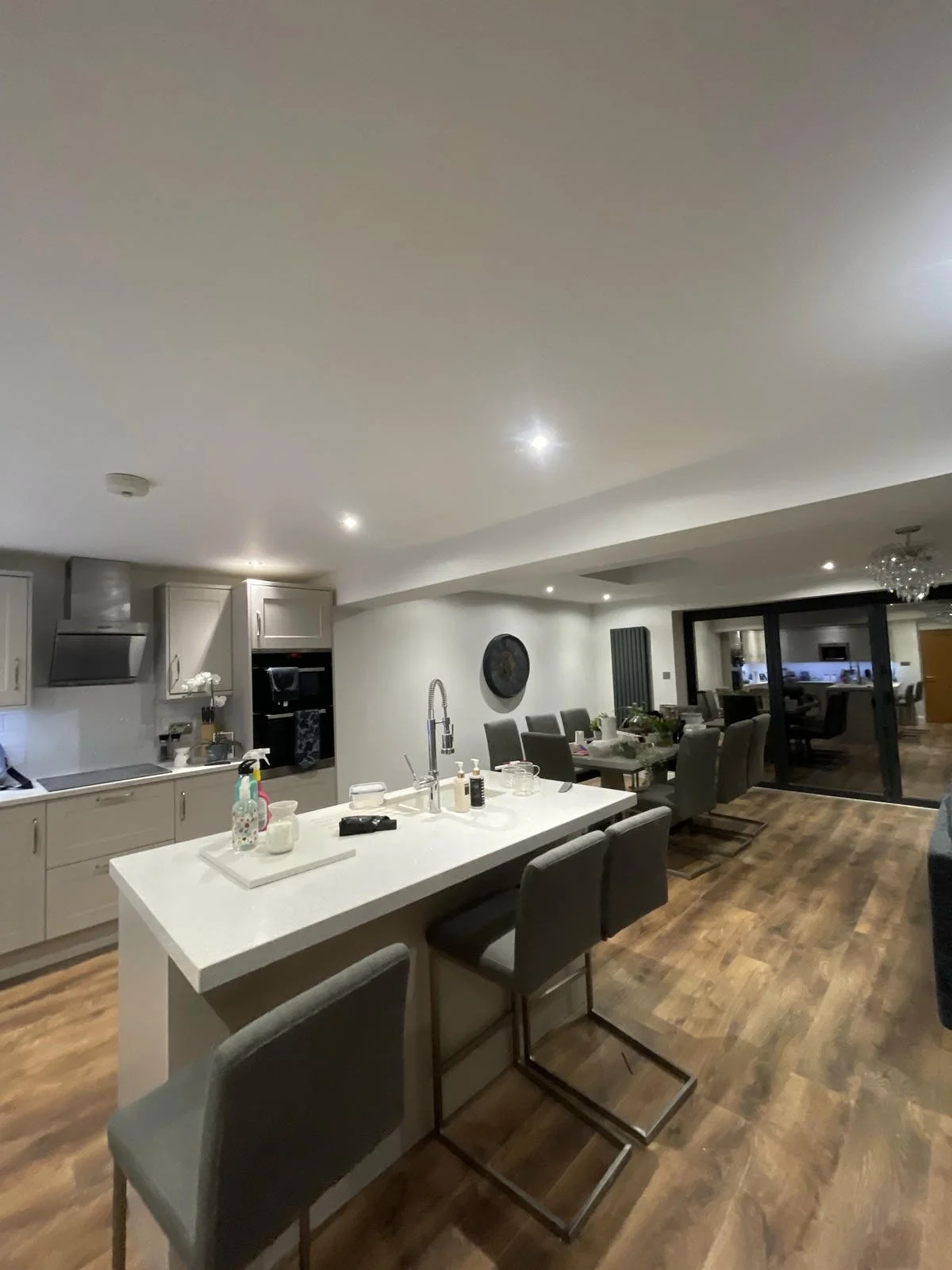 Modern kitchen and dining area with a white island, gray chairs, and hardwood floors, seen through sliding glass doors.