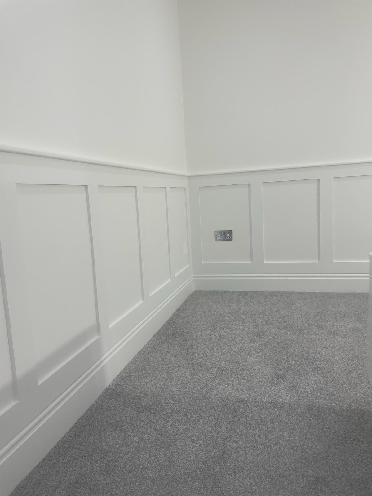 Empty room with white paneled walls, gray carpet, and electrical outlets.
