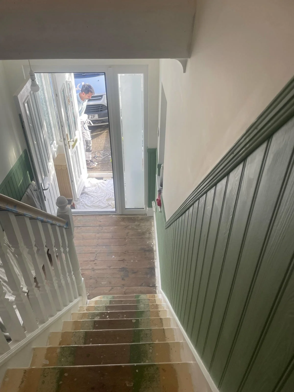 View from top of a staircase looking down at the hallway and front door of a house with a person standing outside.