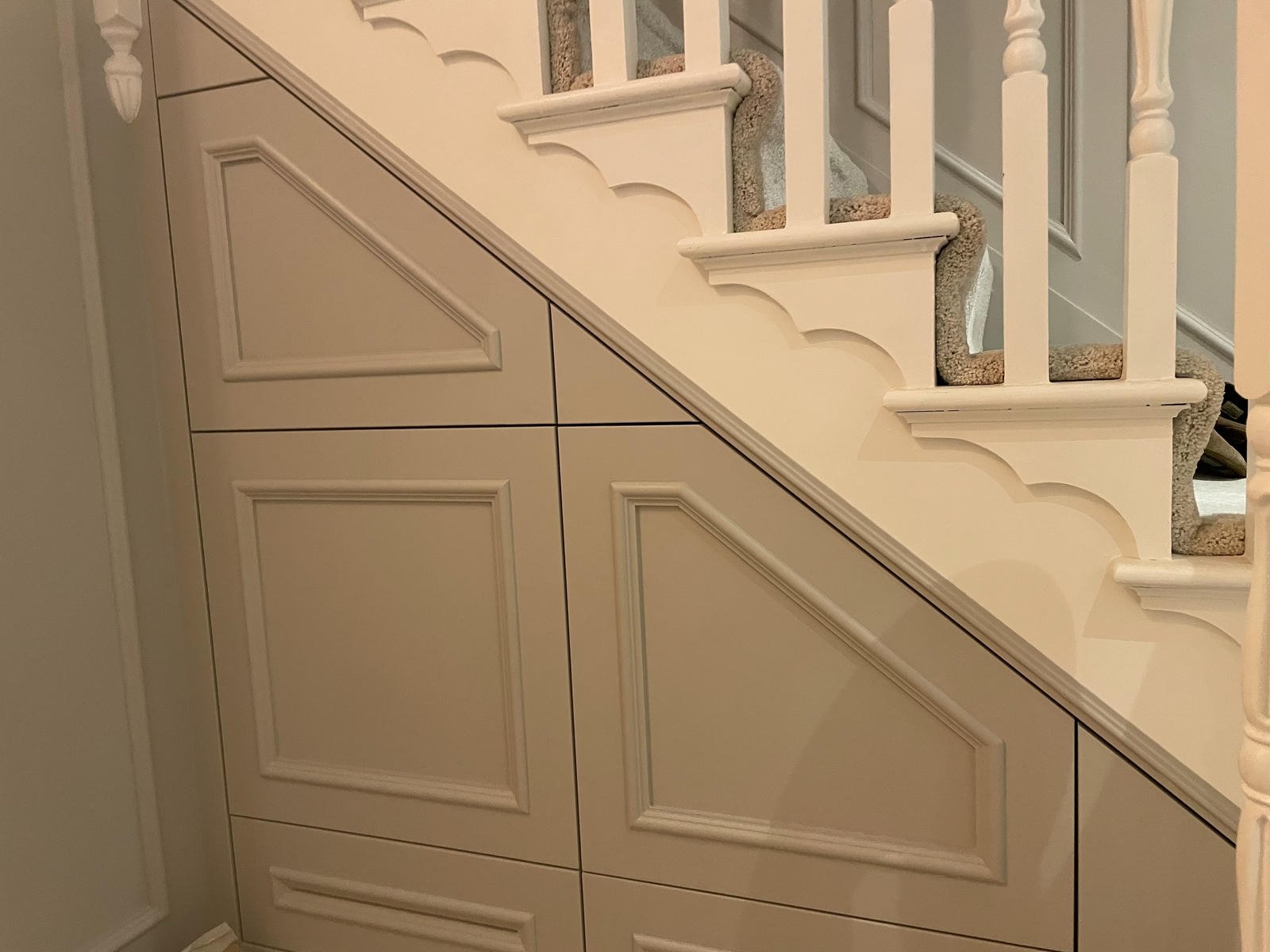 Interior view of a staircase with white wooden banisters and beige carpeted steps, adjacent to a beige paneled wall with decorative moldings.