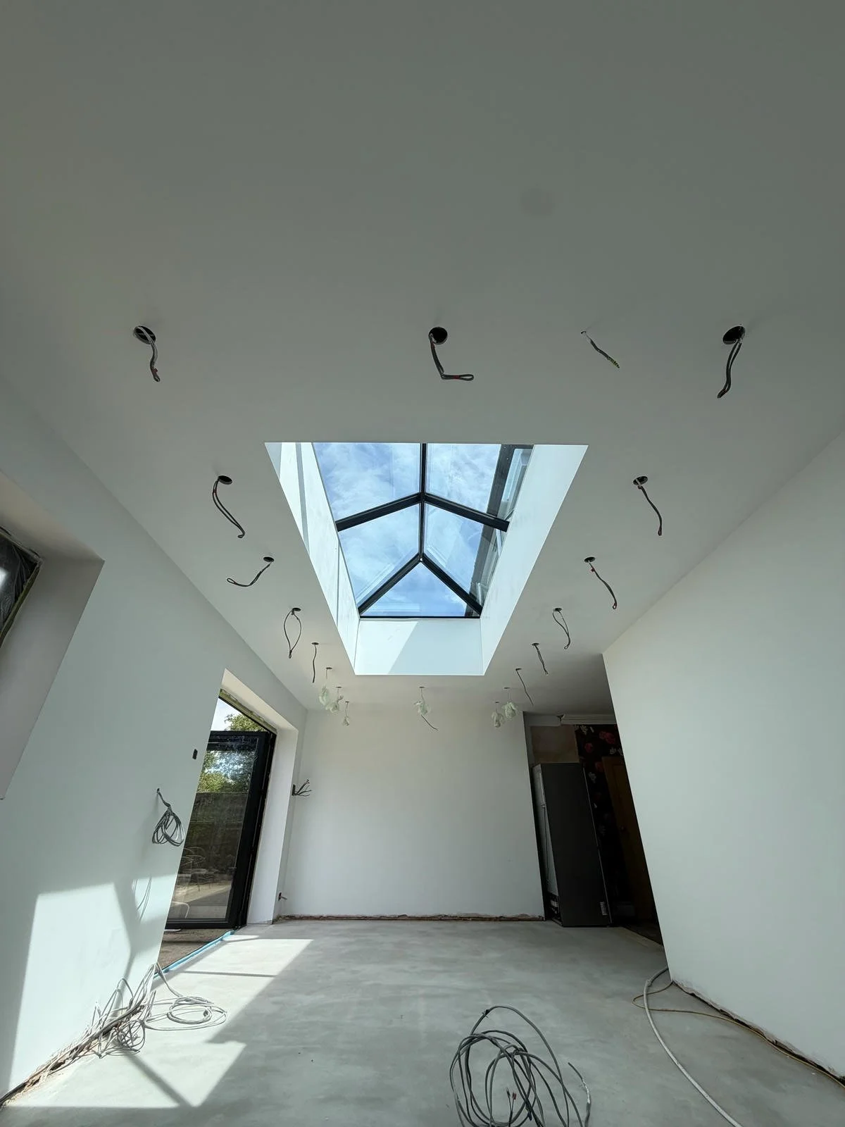 Interior of a room under construction with ceiling wiring, a large skylight, and natural daylight coming through.