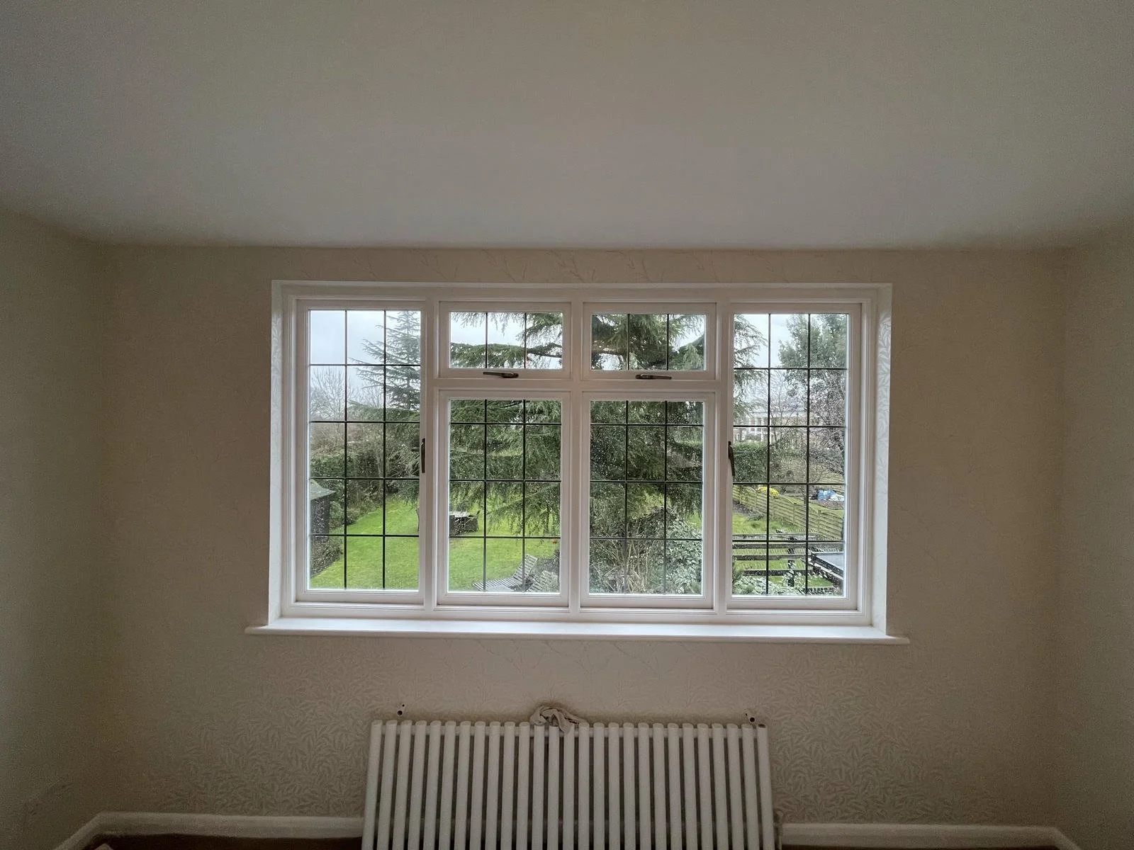 Interior view of a room with a large window overlooking a garden with trees and a lawn, sitting above a white radiator.