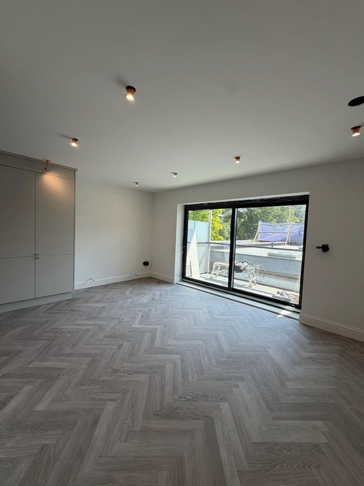 Empty room with wood flooring, white walls, large sliding glass door, and a view of a balcony under construction.