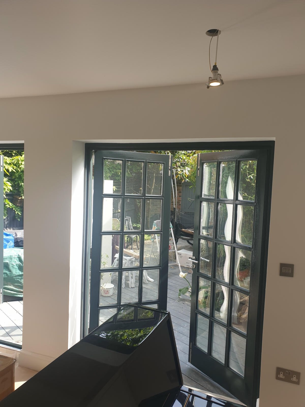 Interior view of a room with open French doors leading to a backyard garden with trees and outdoor furniture.