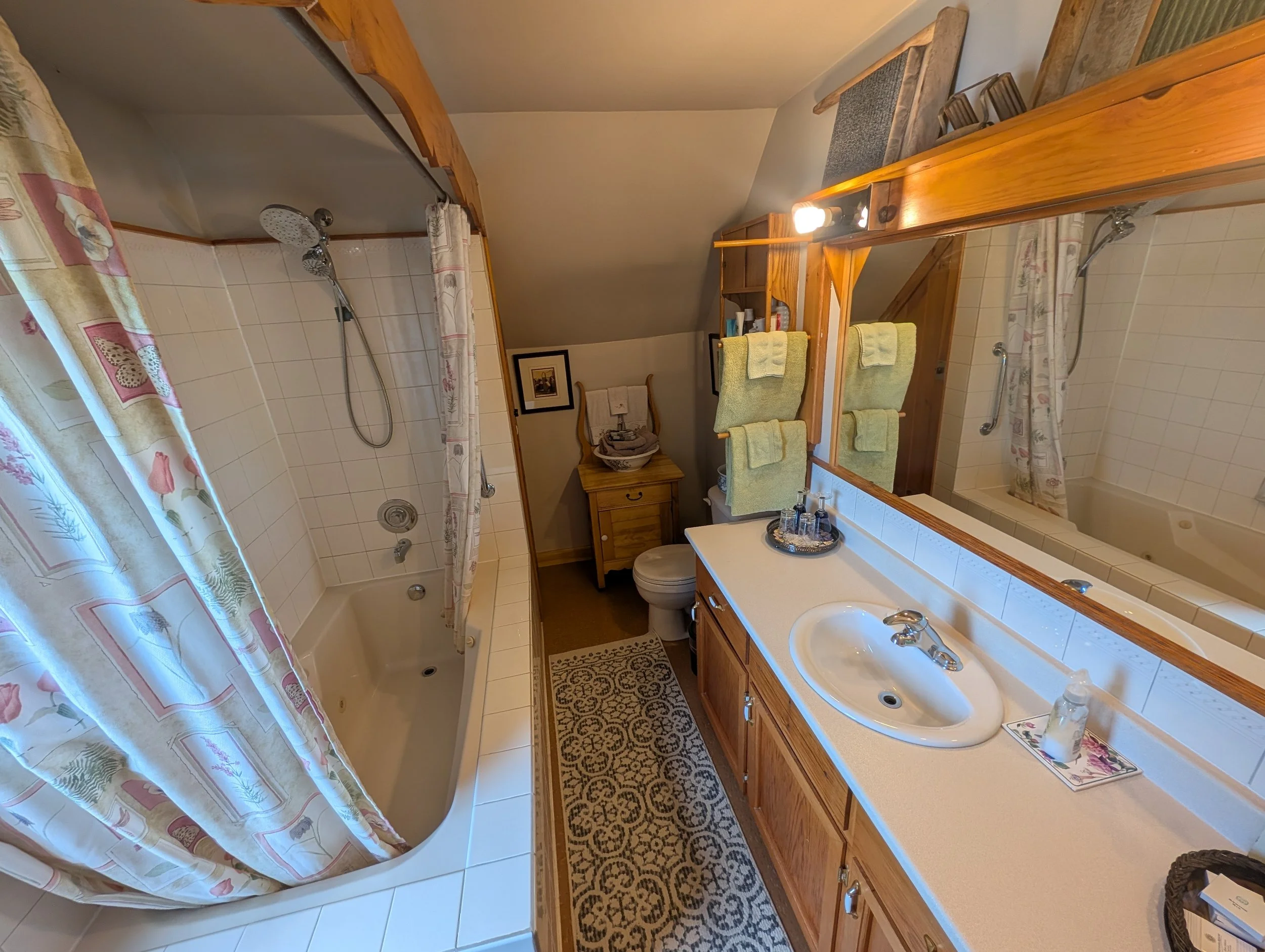 A bathroom with a walk-in shower, yellow towels, wooden cabinets, and a large mirror.