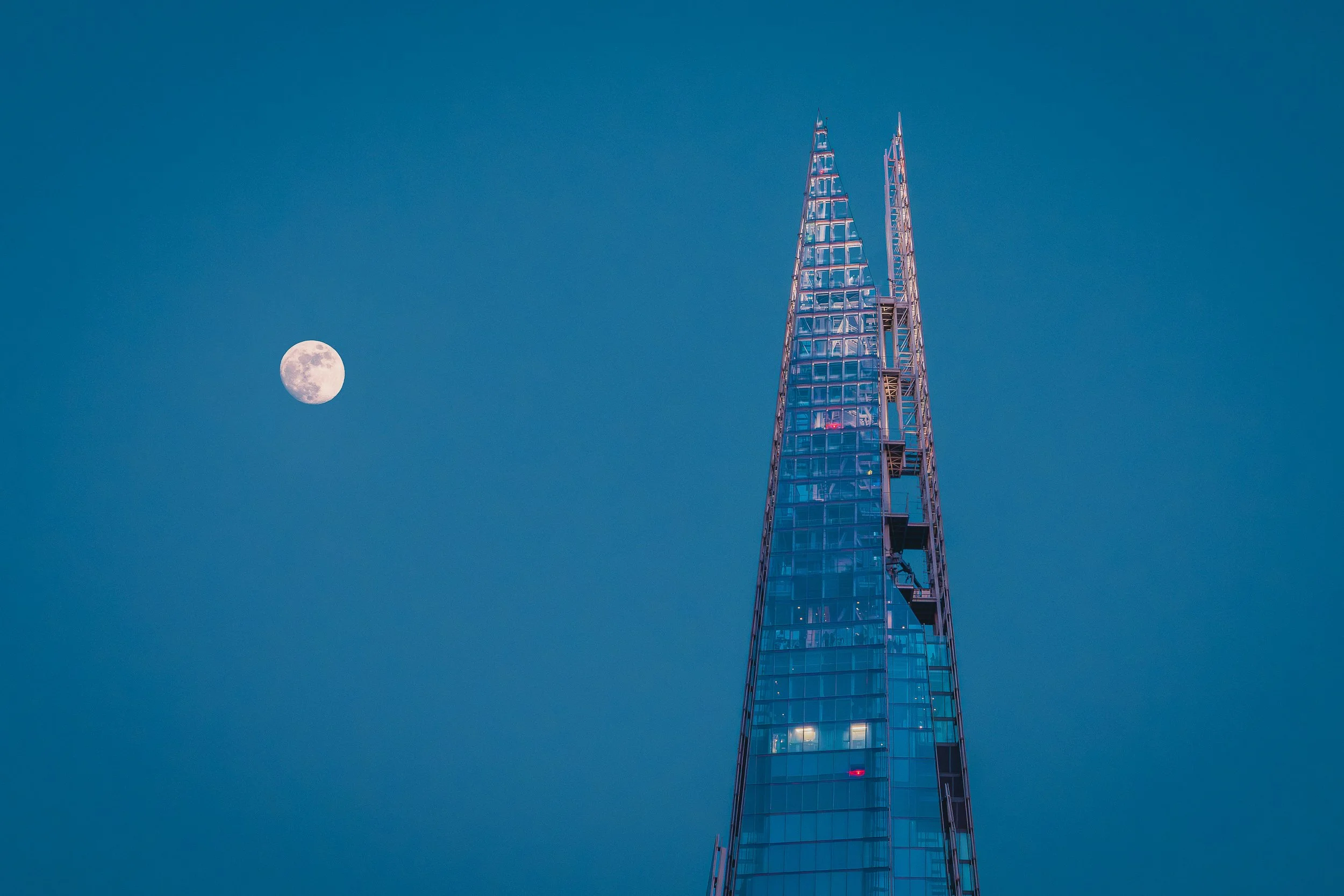 The Shard rising into a deep blue sky with the moon beside it