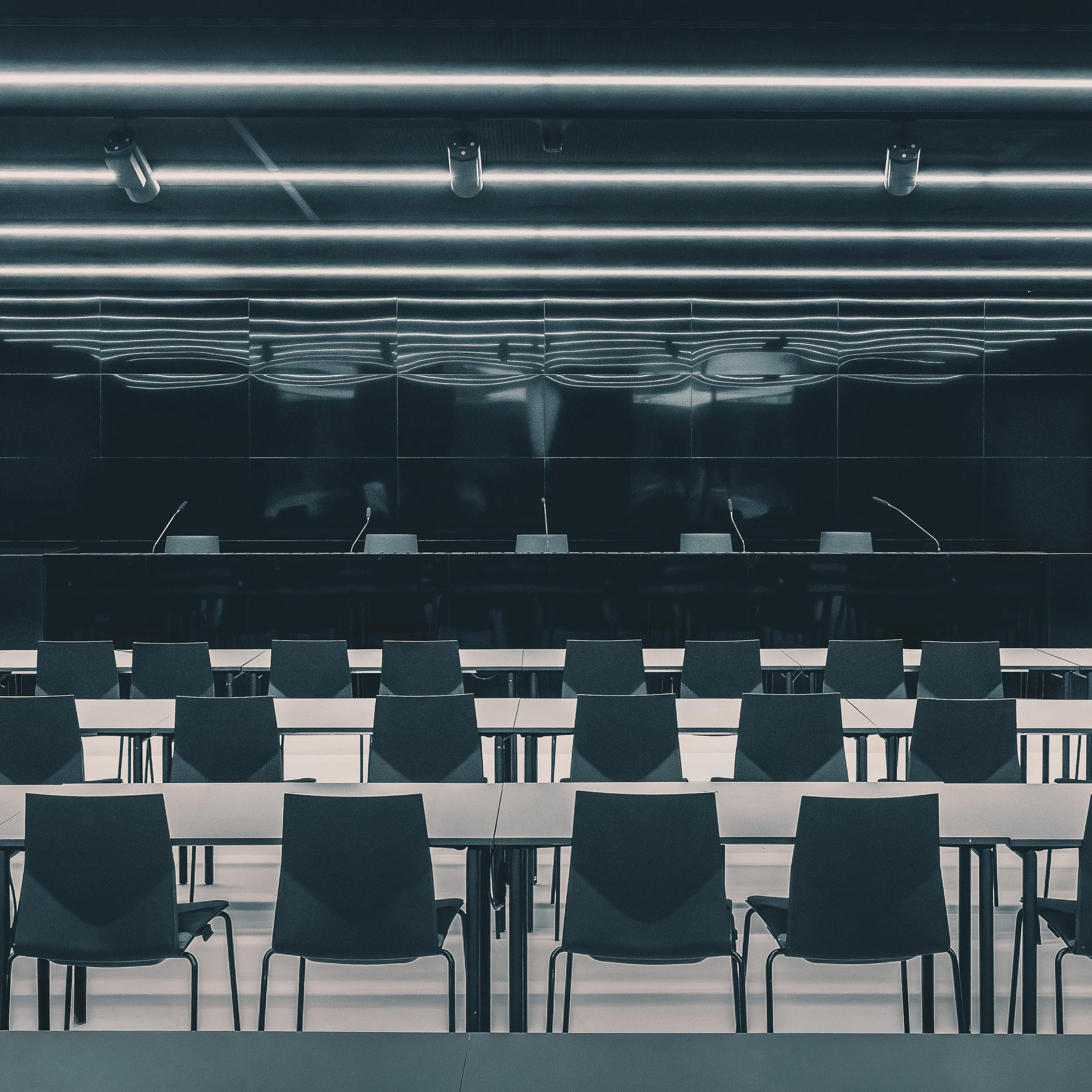 Rows of black chairs and white desks reflected in a dark press room