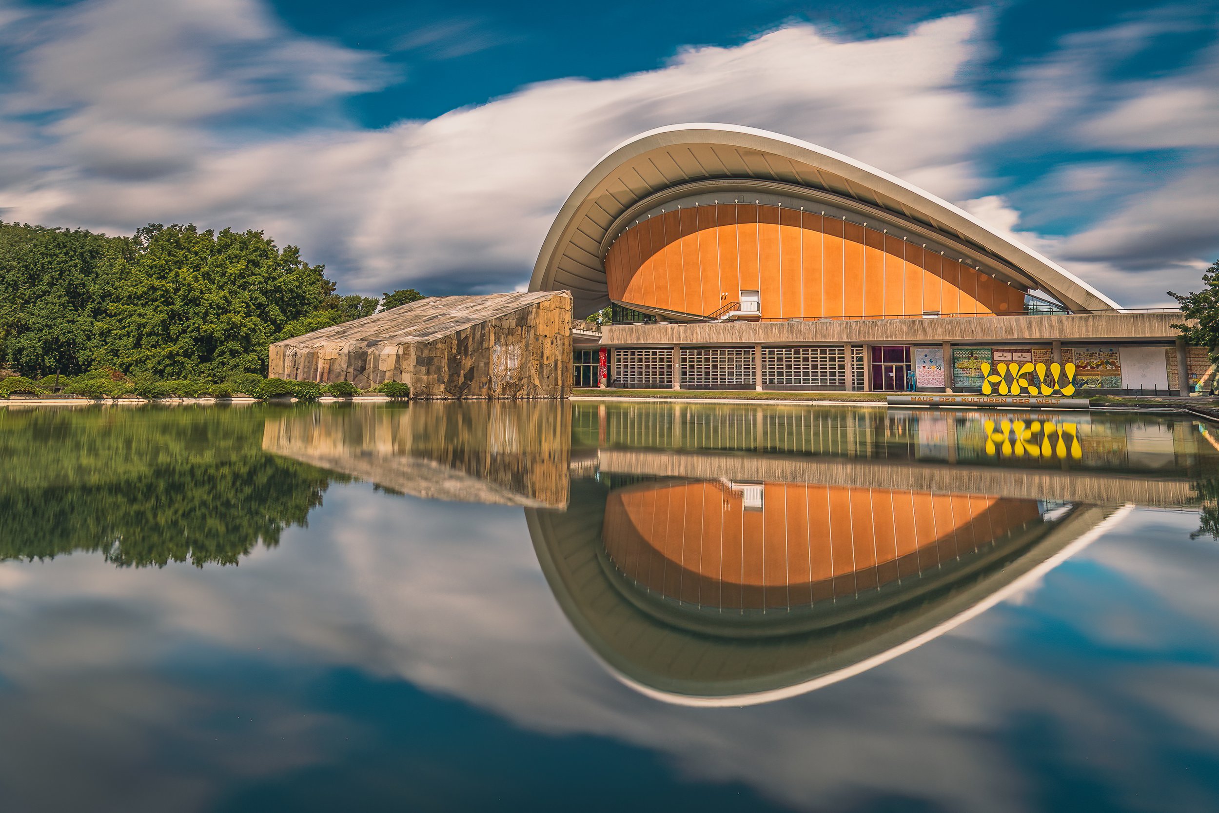 Curved modern haus der Kulturen der Welt reflected in calm water beneath a dramatic sky
